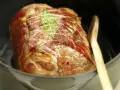 Un rôti de porc cocotte, doré et savoureux, est prêt à cuire dans sa cocotte avec une feuille de laurier et une cuillère en bois.