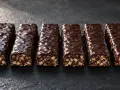 Six barres protéinées maison, enrobées de chocolat noir craquelé, sur fond sombre.