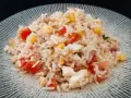 Une généreuse portion de salade de riz thon, garnie de dés de tomates, de maïs et d'œufs durs, sur une assiette texturée.