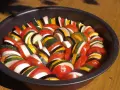Un plat de légumes coupés en rondelles, prêt pour une recette de ratatouille digne du film. Tomates, courgettes, aubergines et oignons s'alternent.