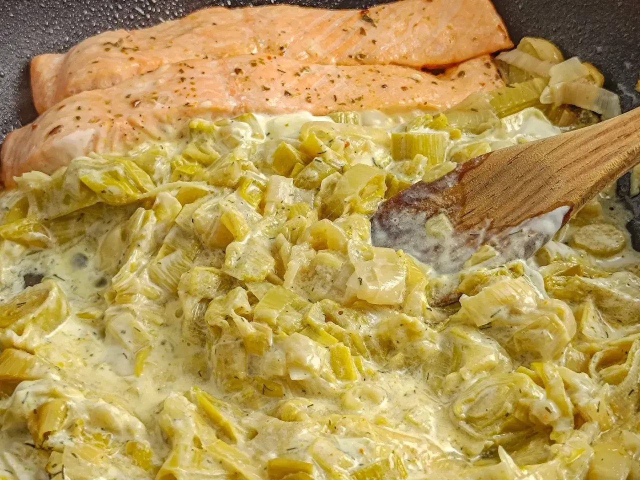 Filets de saumon poêlés sur une fondue de poireaux crémeuse, mélangée avec une cuillère en bois.
