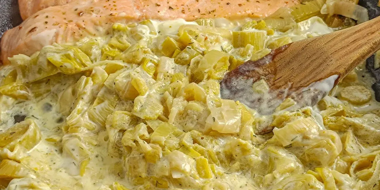 Filets de saumon poêlés sur une fondue de poireaux crémeuse, mélangée avec une cuillère en bois.