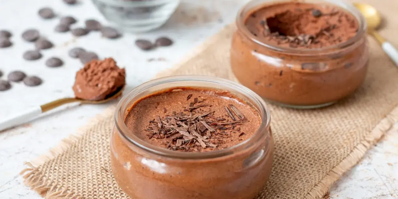 Deux pots de mousse au chocolat, garnie de copeaux de chocolat, sur une toile de jute. Une cuillère dorée est remplie de cette délicieuse mousse.