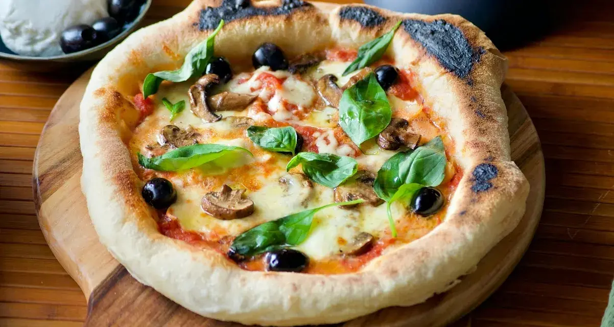 Pizza maison avec une pâte à pizza dorée, garnie de champignons, olives noires et basilic frais. Un délice !