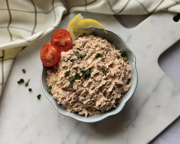 Un bol de rillettes de thon, garni de tomates cerises et de quartiers de citron, prêt à être dégusté.