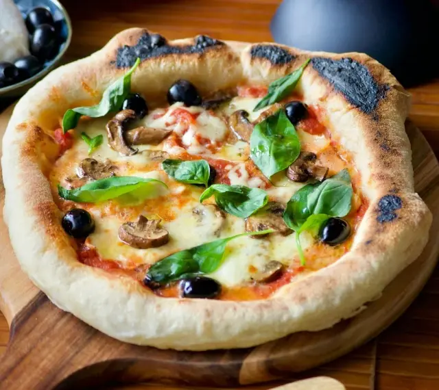 Pizza maison avec une pâte à pizza dorée, garnie de champignons, olives noires et basilic frais. Un délice !