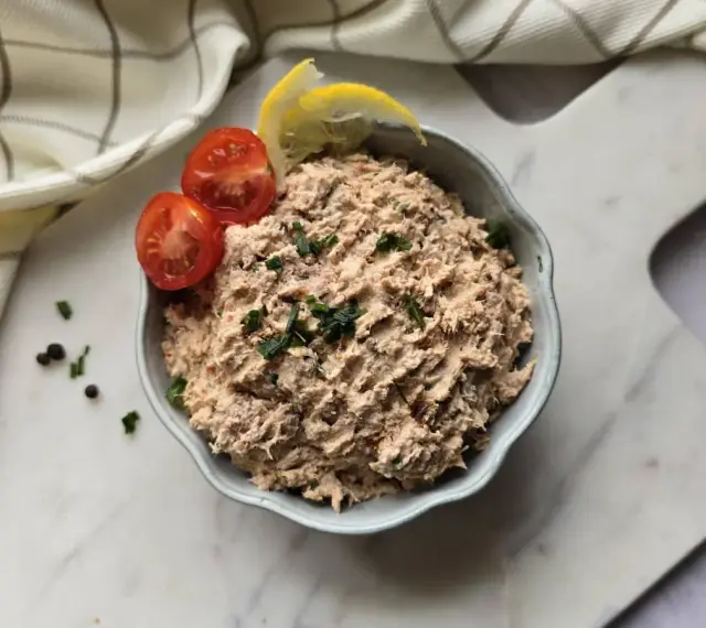 Un bol de rillettes de thon, garni de tomates cerises et de quartiers de citron, prêt à être dégusté.