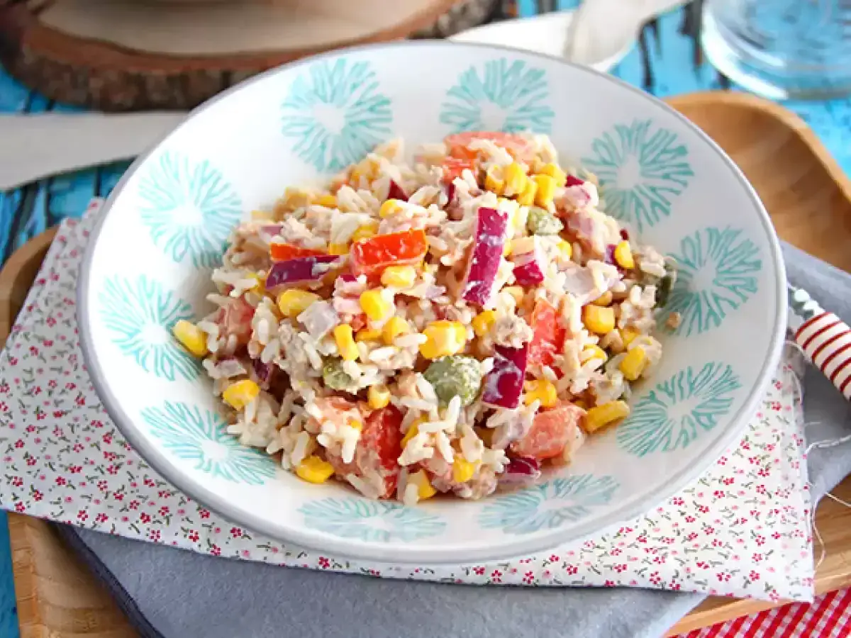 Salade de riz colorée avec maïs, tomates, poivrons rouges et oignons, servie dans un bol décoré.