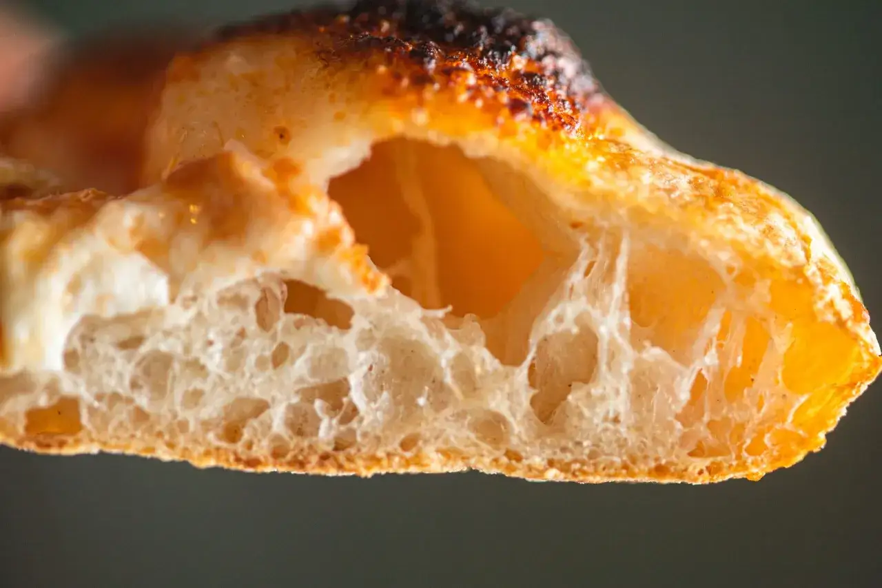 Gros plan sur la mie aérée et dorée d'une pâte à pizza, avec une croûte légèrement brûlée.