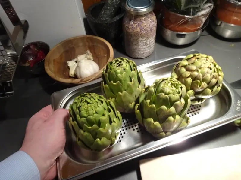 Quatre artichauts verts prêts pour la cuisson vapeur. Une main tient le plateau.