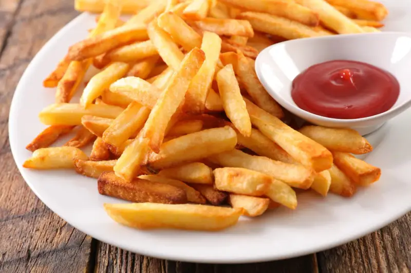 Une assiette de frites au four dorées et croustillantes, accompagnées d'un petit bol de ketchup rouge vif.