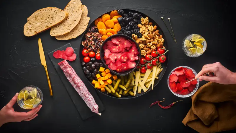 Planche apéro généreuse : charcuterie, fruits secs, olives, tomates, fromage, cornichons et pain. Une belle idée pour un moment convivial.