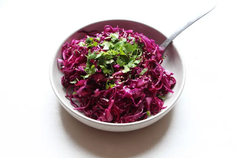 Salade colorée de chou rouge râpé, garnie de coriandre fraîche et de graines de sésame. Une idée simple pour une recette chou rouge savoureuse.