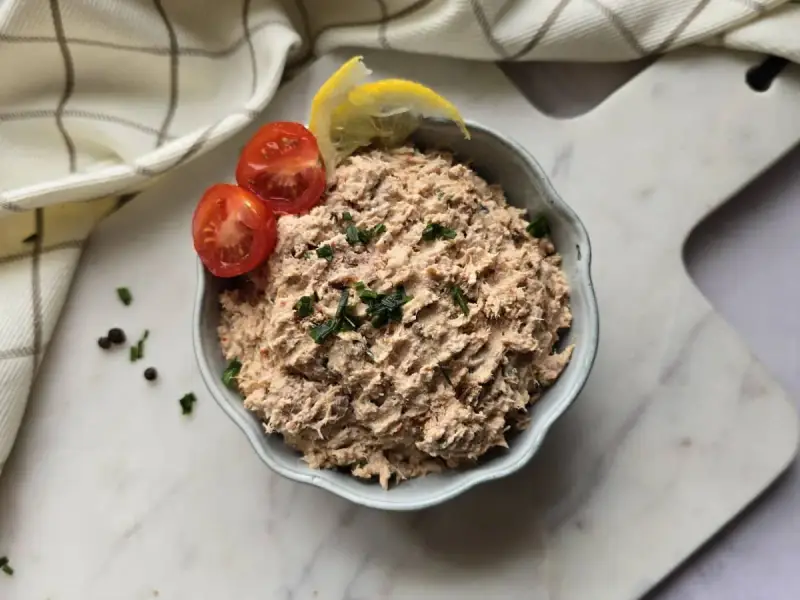 Un bol de rillettes de thon, garni de tomates cerises et de quartiers de citron, prêt à être dégusté.