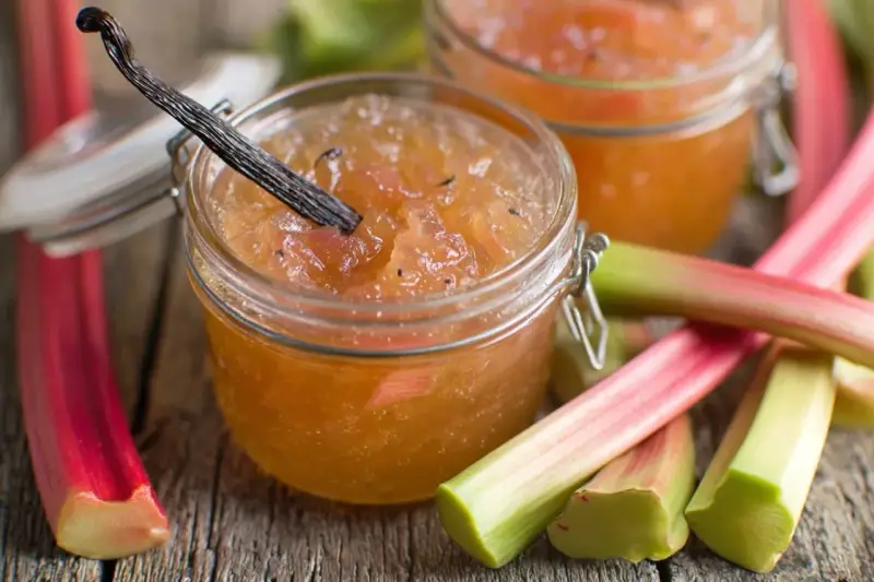 Confiture de rhubarbe maison, avec une gousse de vanille, sur un fond de tiges de rhubarbe fraîches.